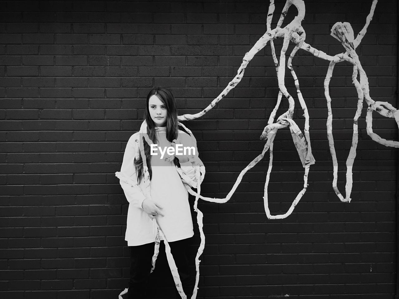 Young woman with ropes standing against brick wall
