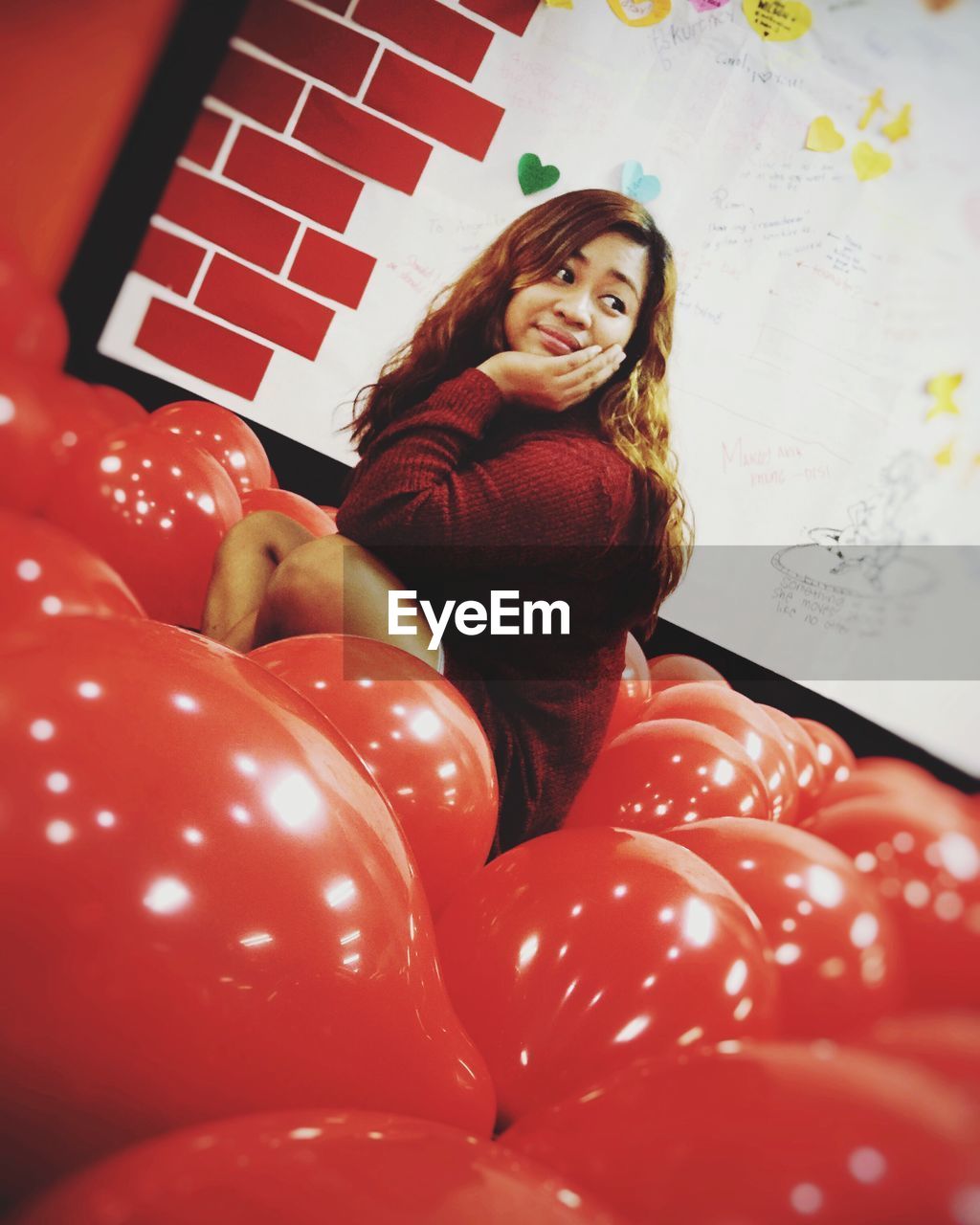 Young woman looking away while sitting amidst red balloons