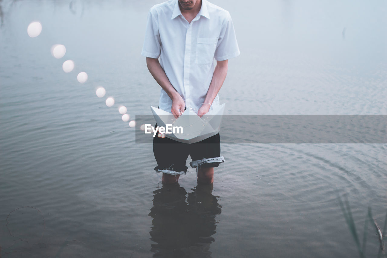 Young man holding paper boat with lights in lake