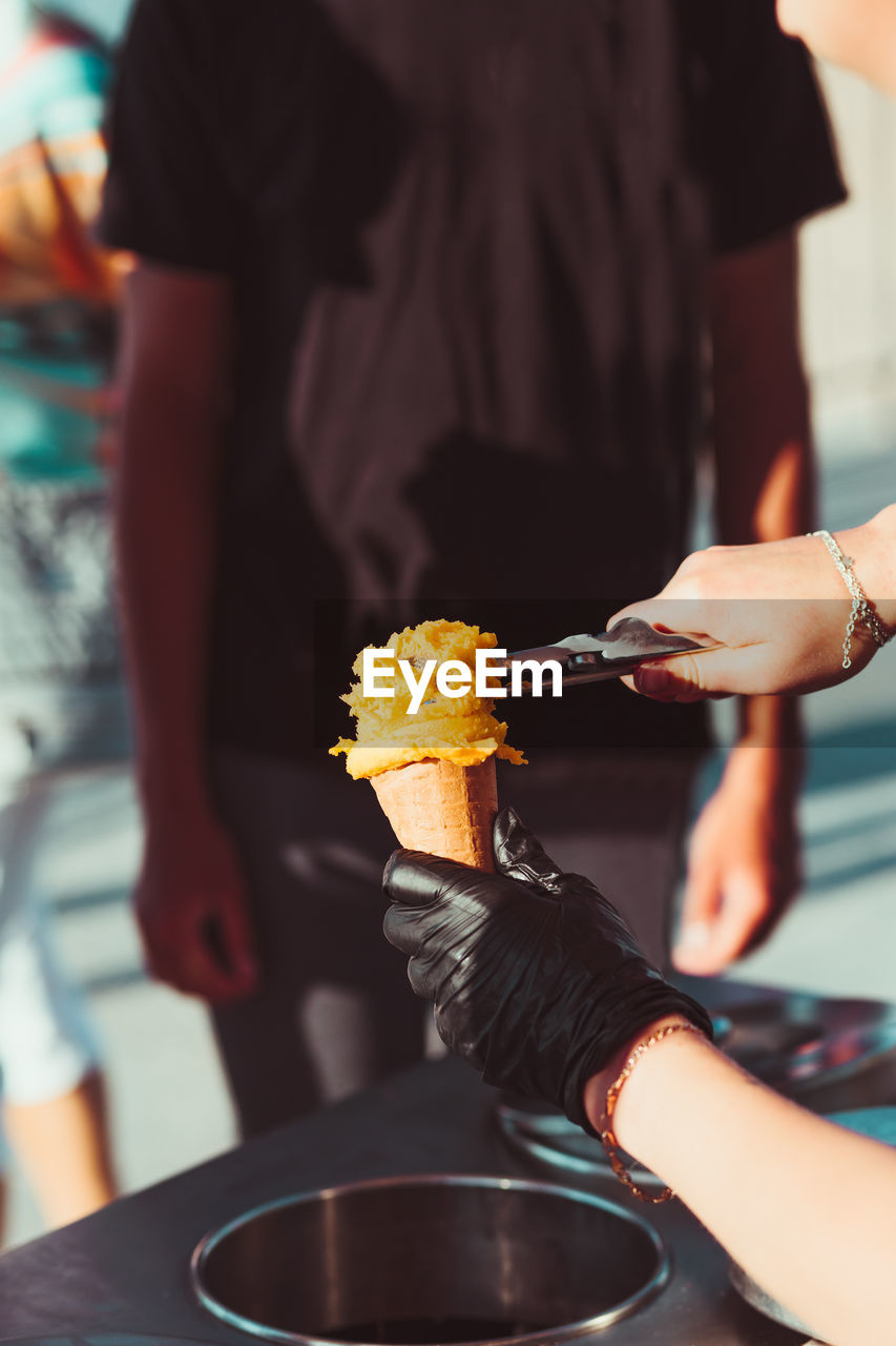 Young boy buying icecream in a candy shop by a street. woman putting a scoop of yellow icecream