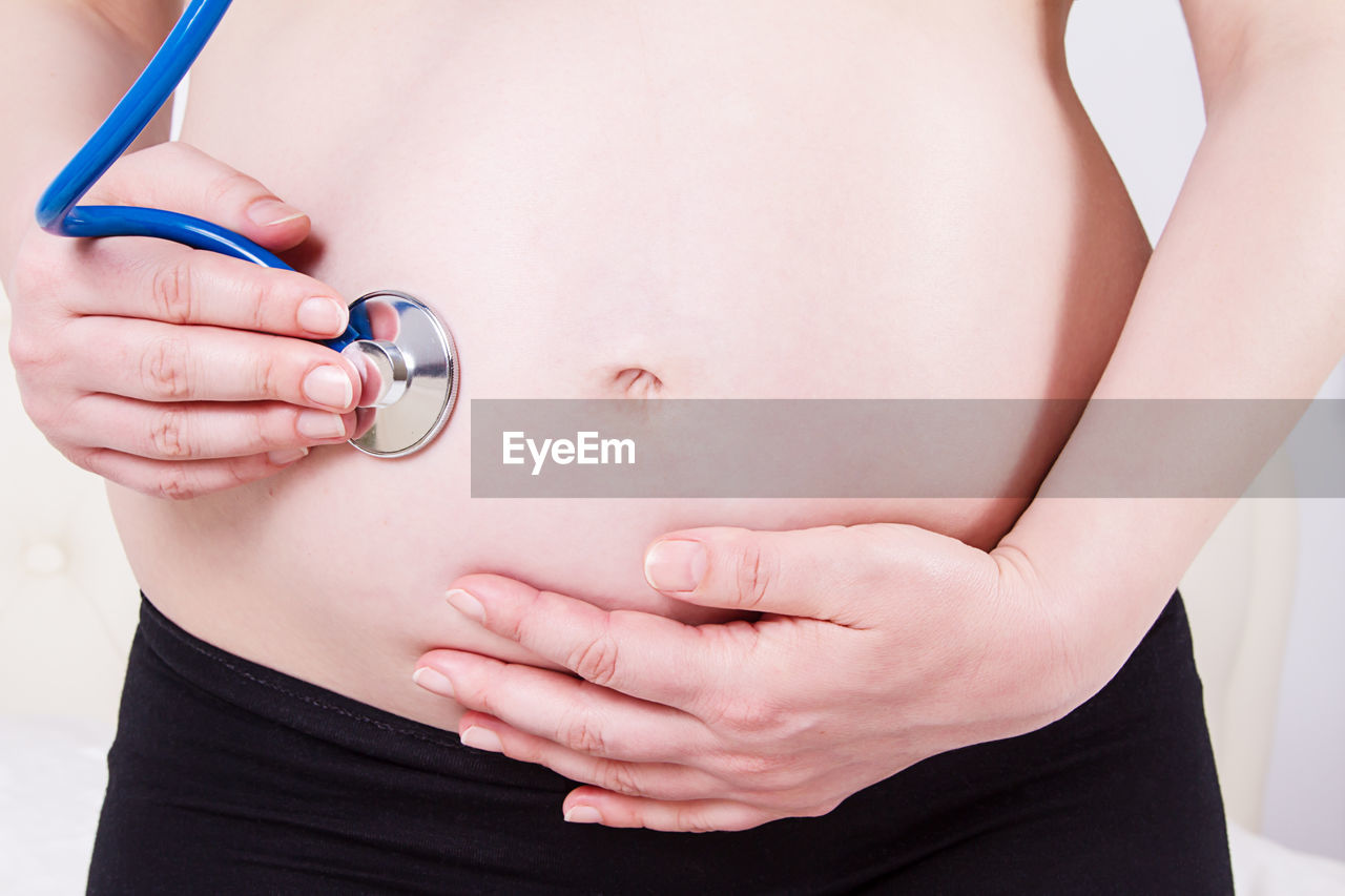 Midsection of pregnant woman examining belly at home
