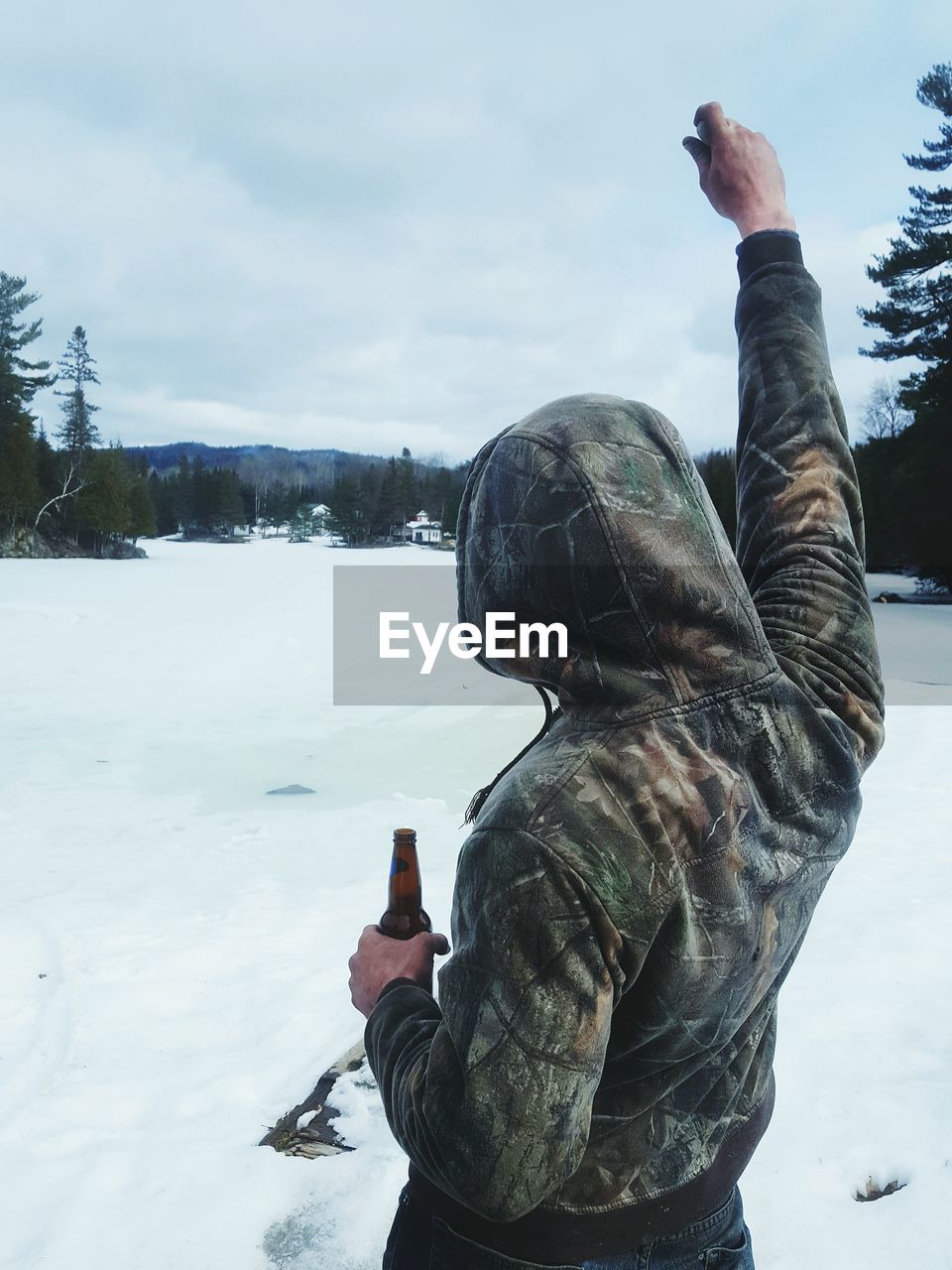 Rear view of man holding bottle by snow covered field