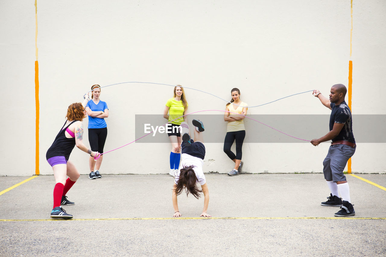Women looking at friends performing double dutch on street