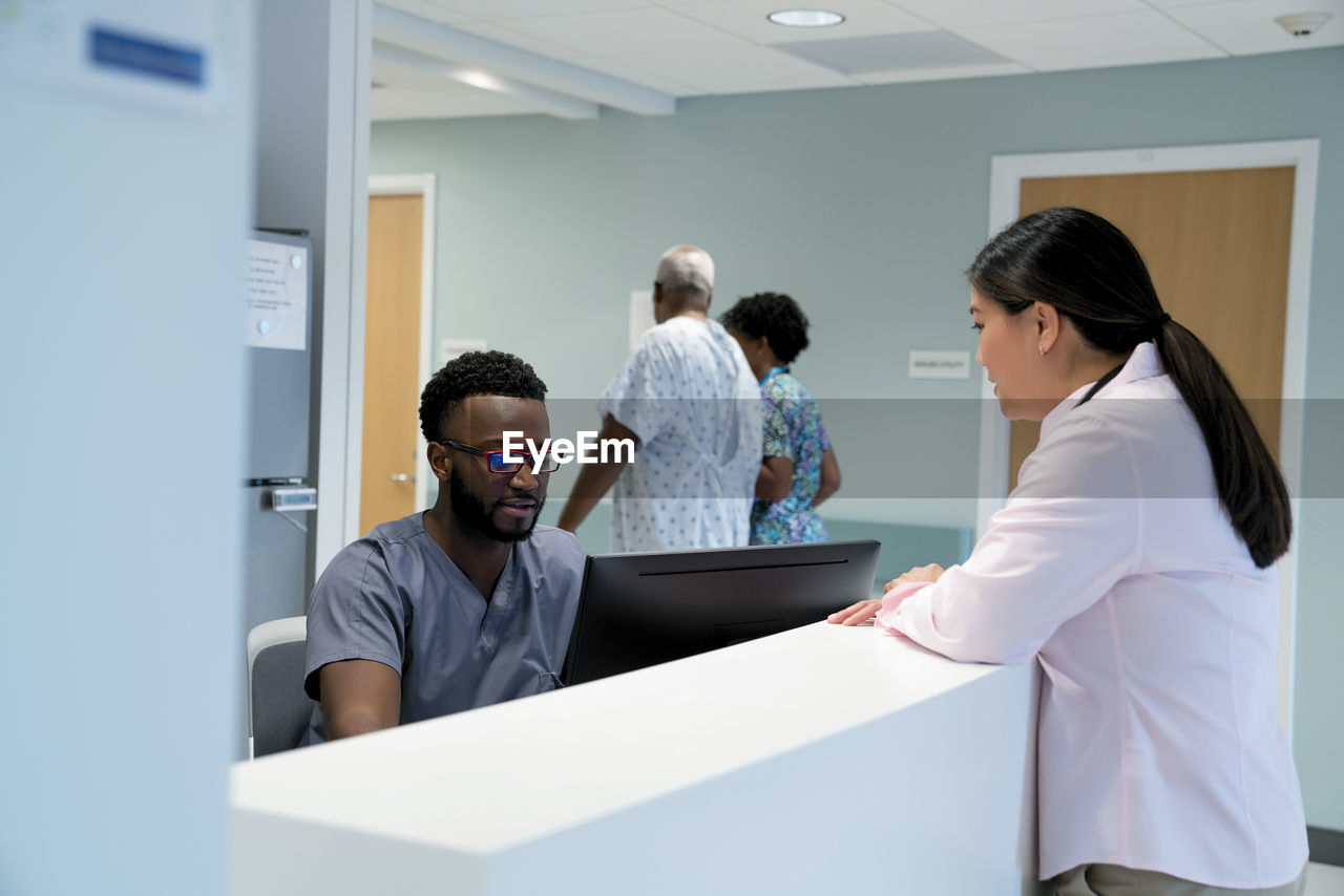Doctor talking to male nurse at hospital reception while colleague with patient walking in background