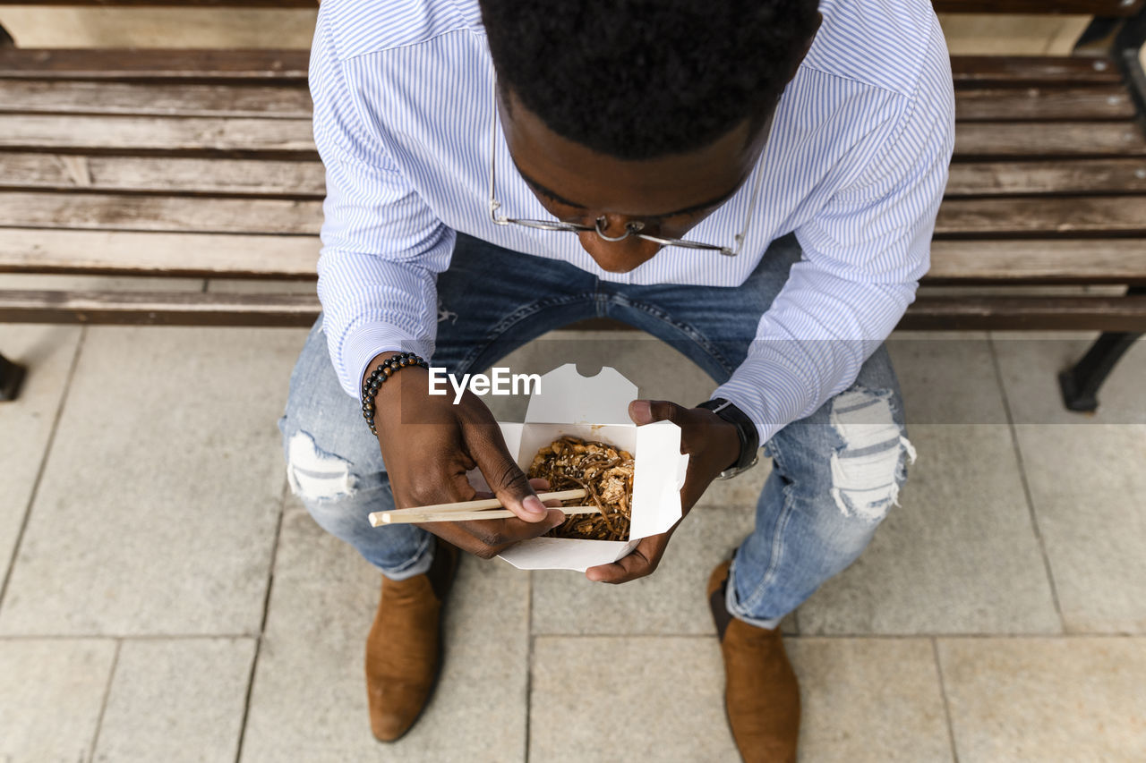 Young man having food sitting on bench