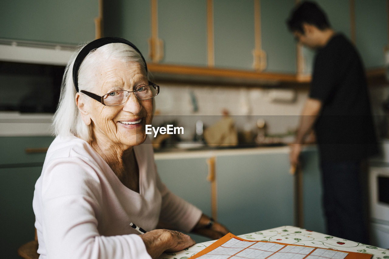 Portrait of smiling senior woman while male caregiver standing in background at home