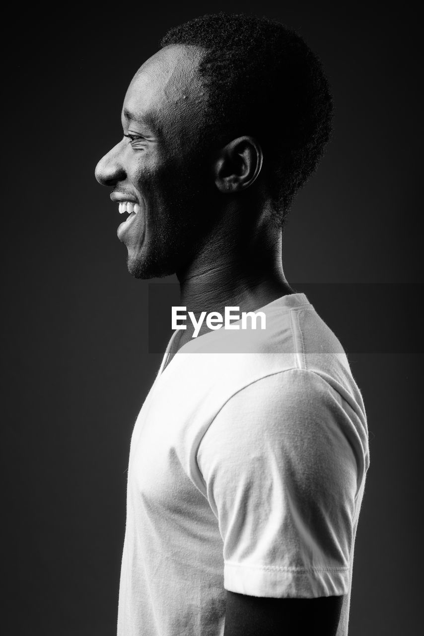 Side view of young man looking away against black background