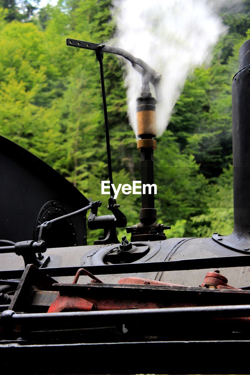 Close-up of steam emitting from locomotive against trees