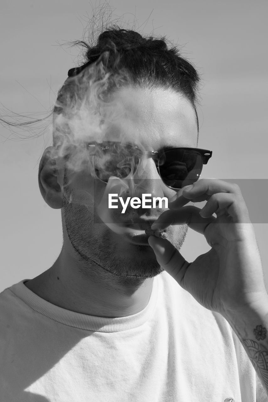 PORTRAIT OF YOUNG MAN SMOKING ON SUNGLASSES AGAINST SKY