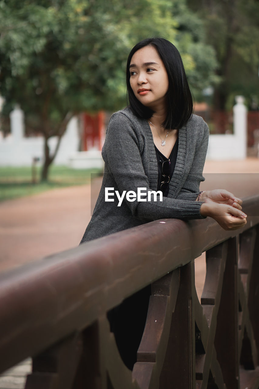 Portrait of young woman sitting on railing