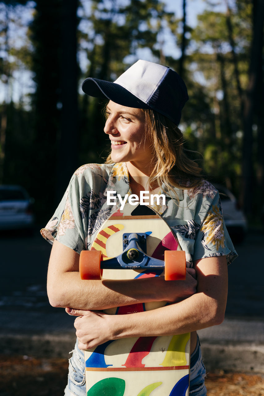 Cheerful woman looking away outdoors while holding skateboard