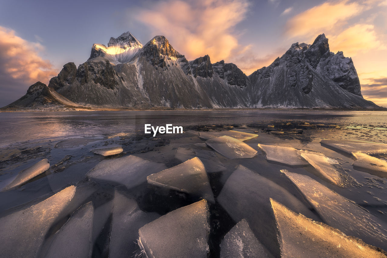 Scenic view of frozen beach against snowy mountains in winter evening in iceland