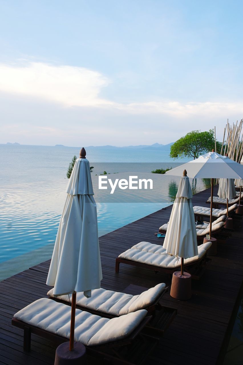 Deck chairs and parasols by infinity pool against sky