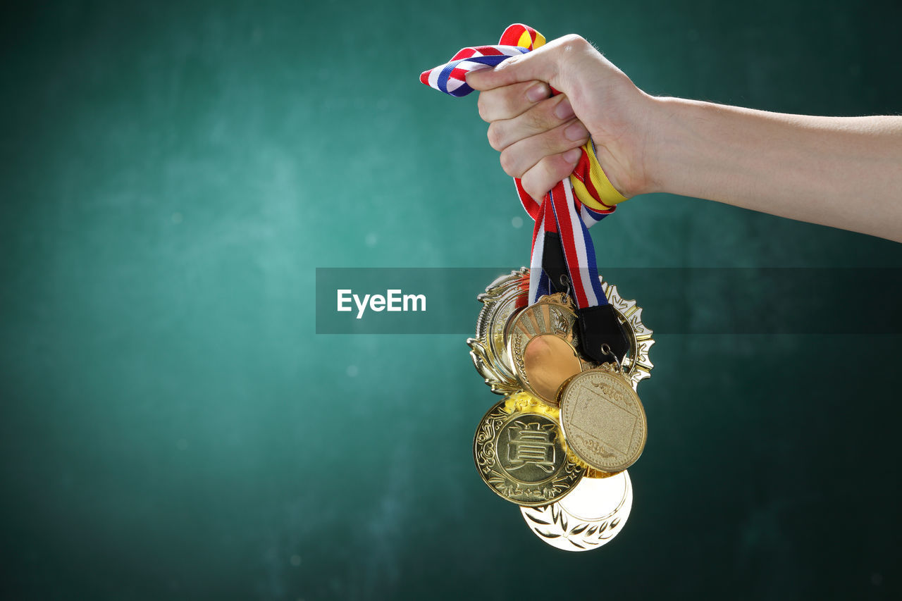 Cropped image of hand holding medals against wall