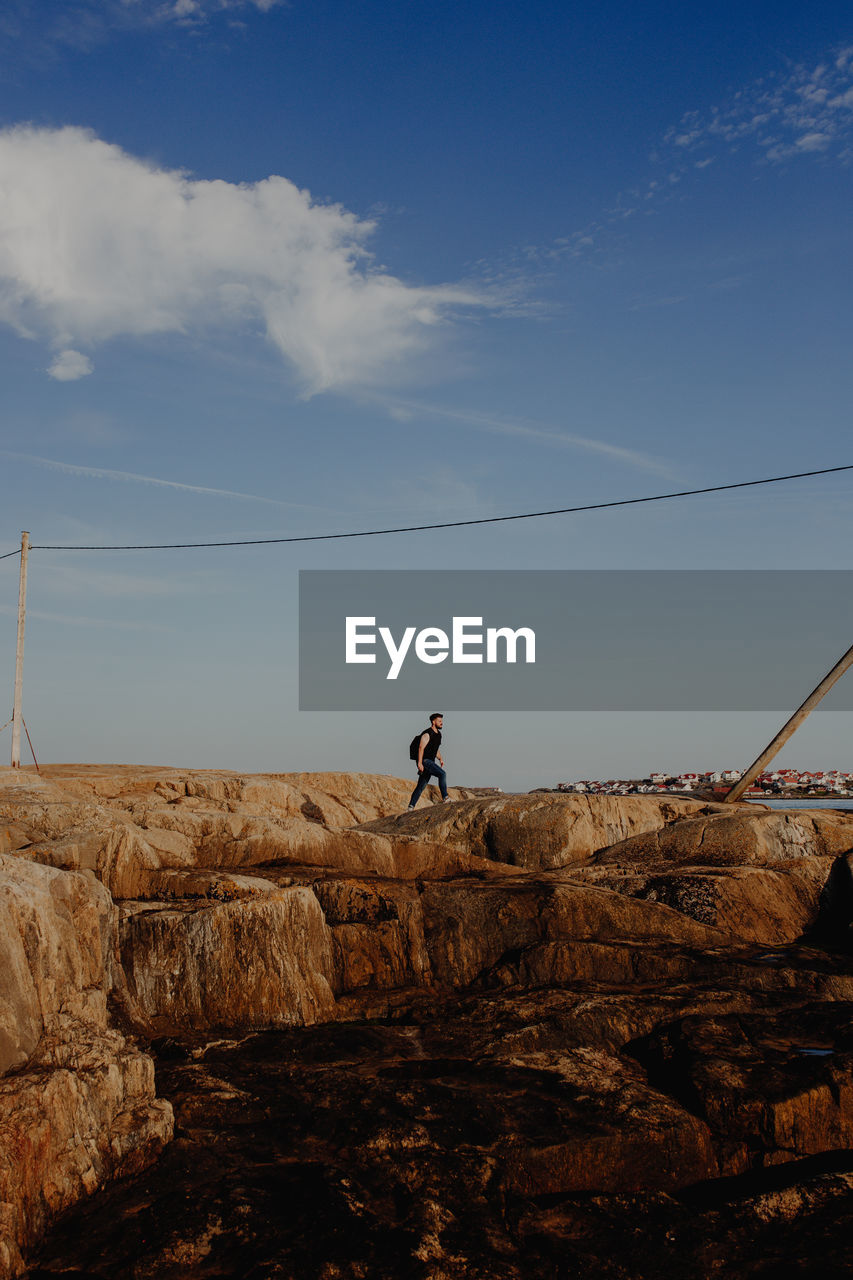 Man on rock formation against sky