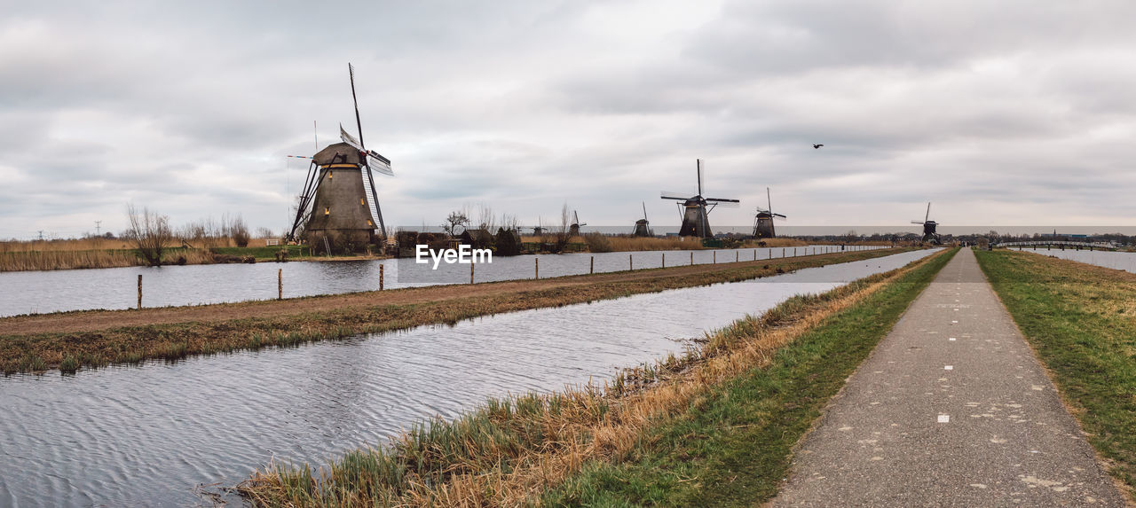 Traditional windmill by canal against sky