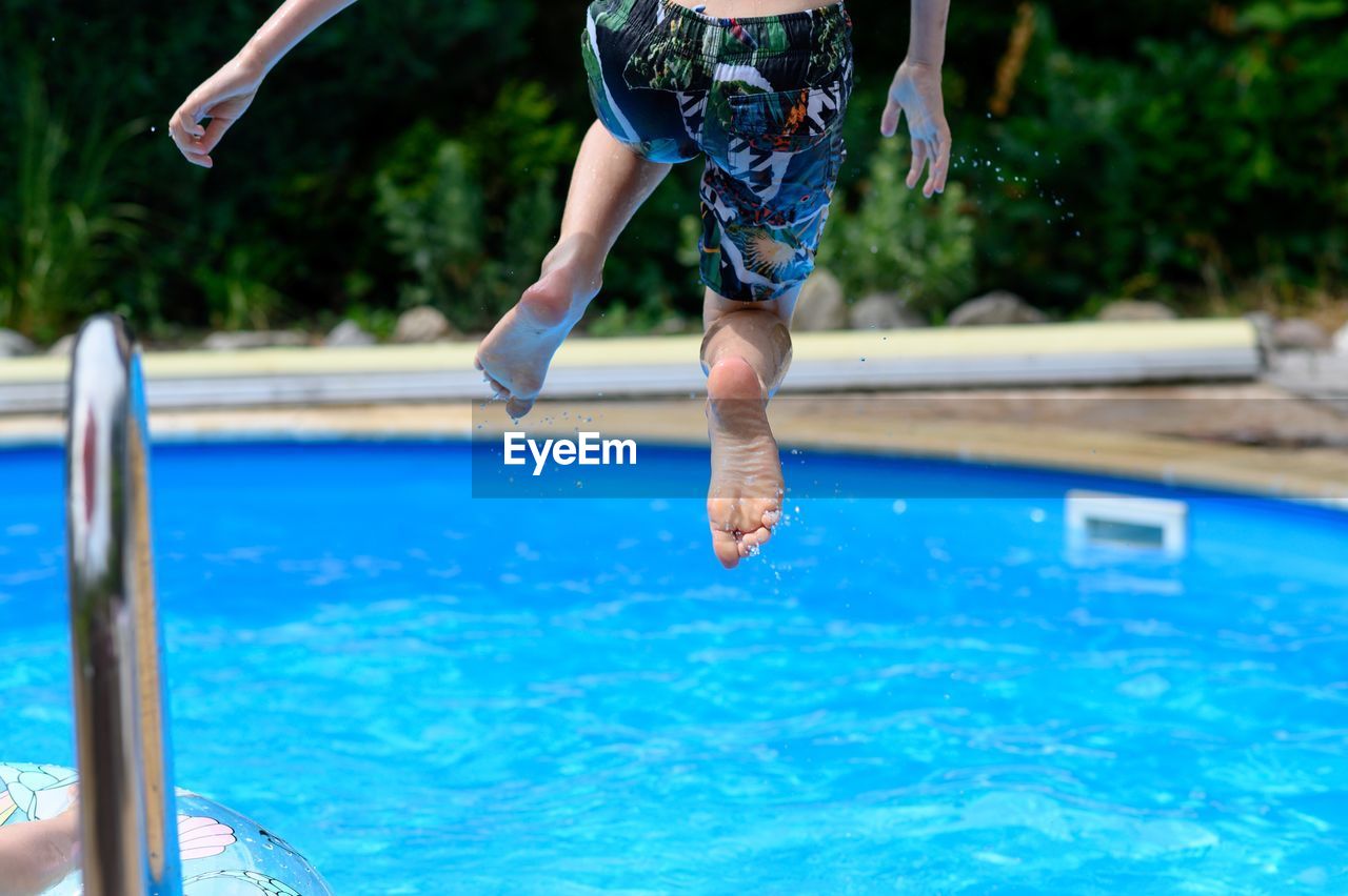 Low section of boy jumping in swimming pool