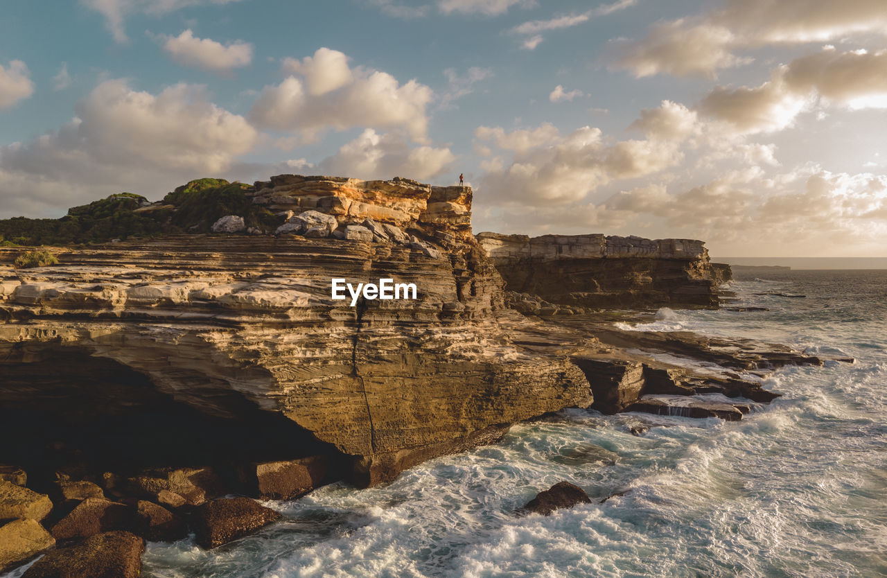 Drone aerial of person standing on massive coastal cliff formation with dramatic morning sky