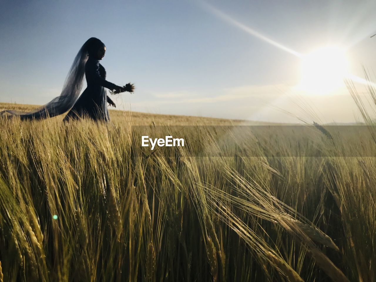 Side view of woman holding crop walking on field