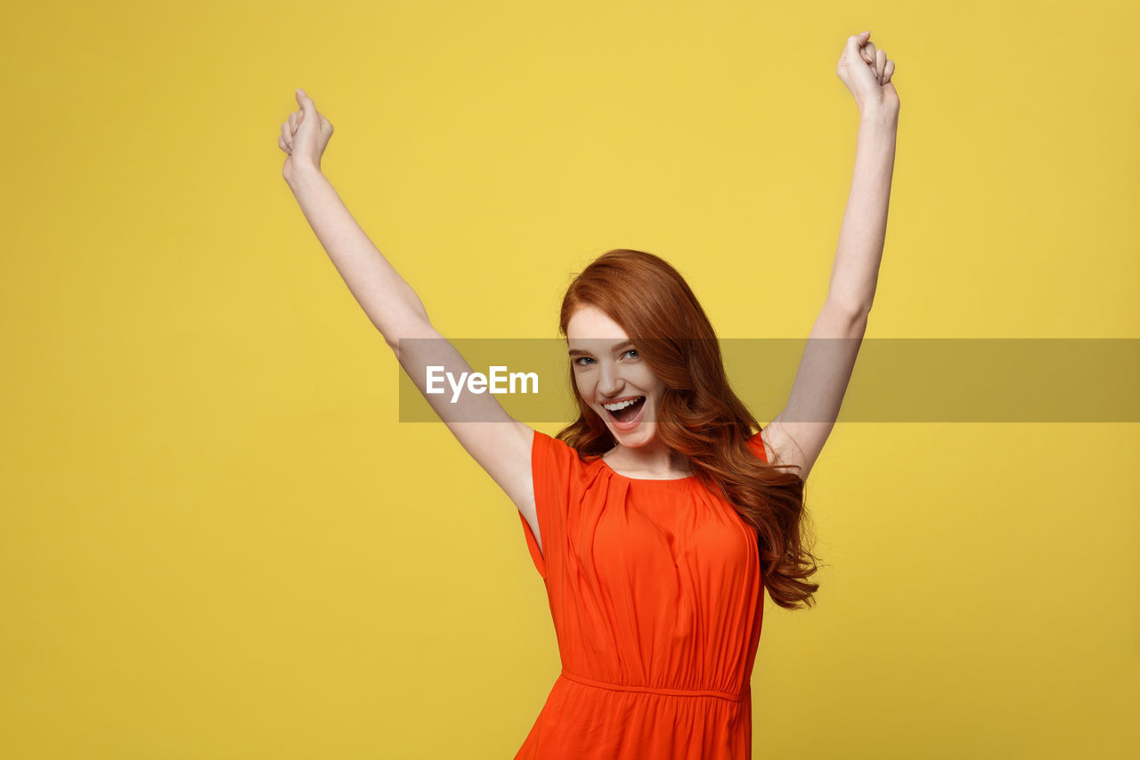 Young woman standing against yellow background