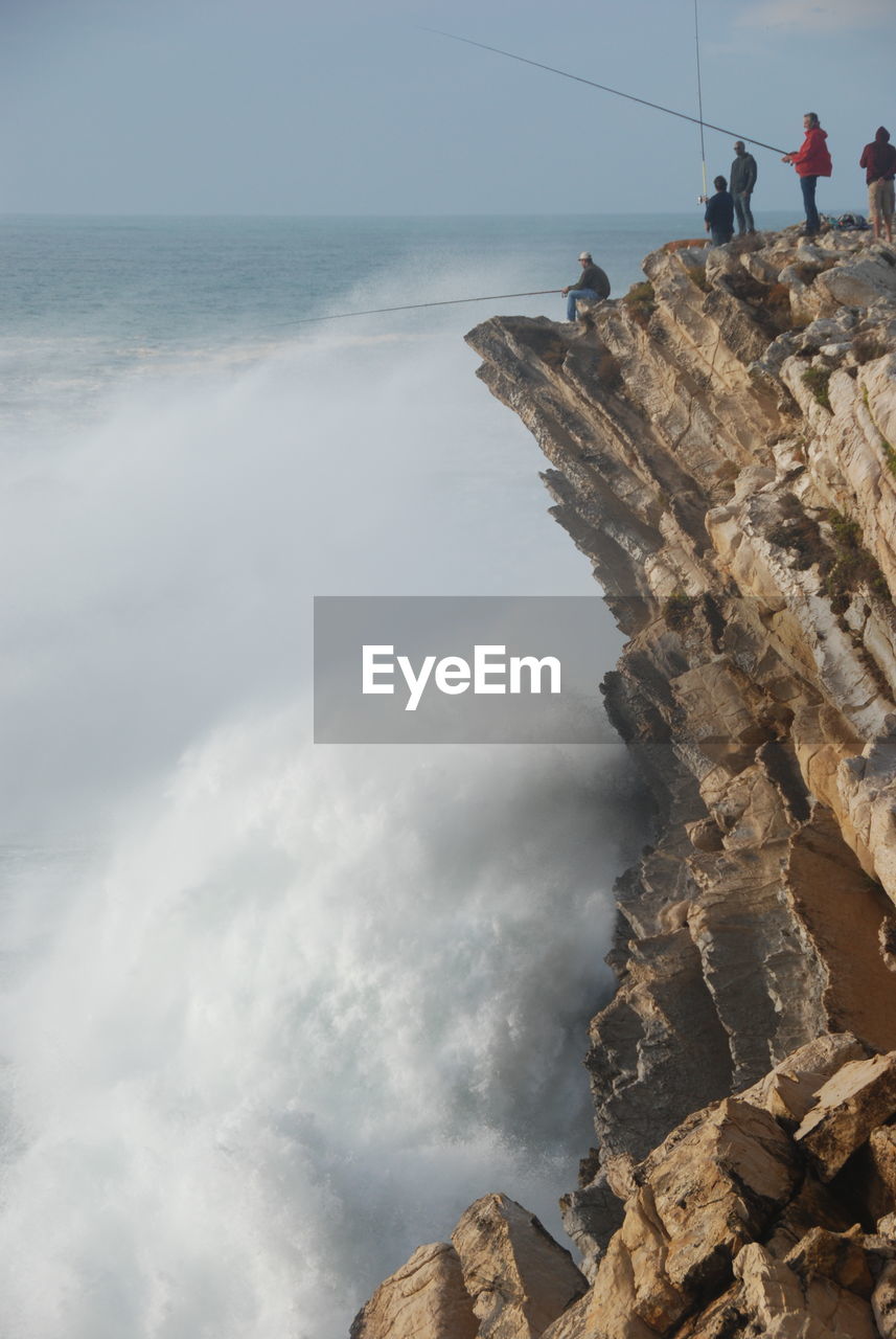People fishing on cliff by splashing sea wave