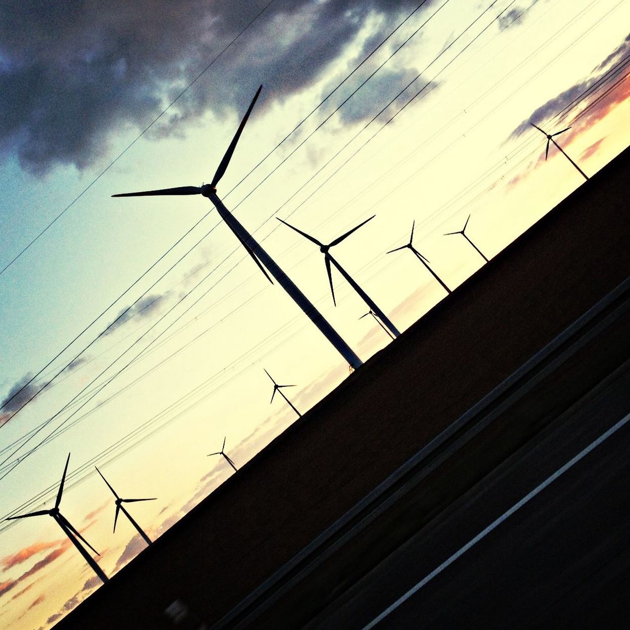 Silhouette wind turbines on landscape against sky at dusk