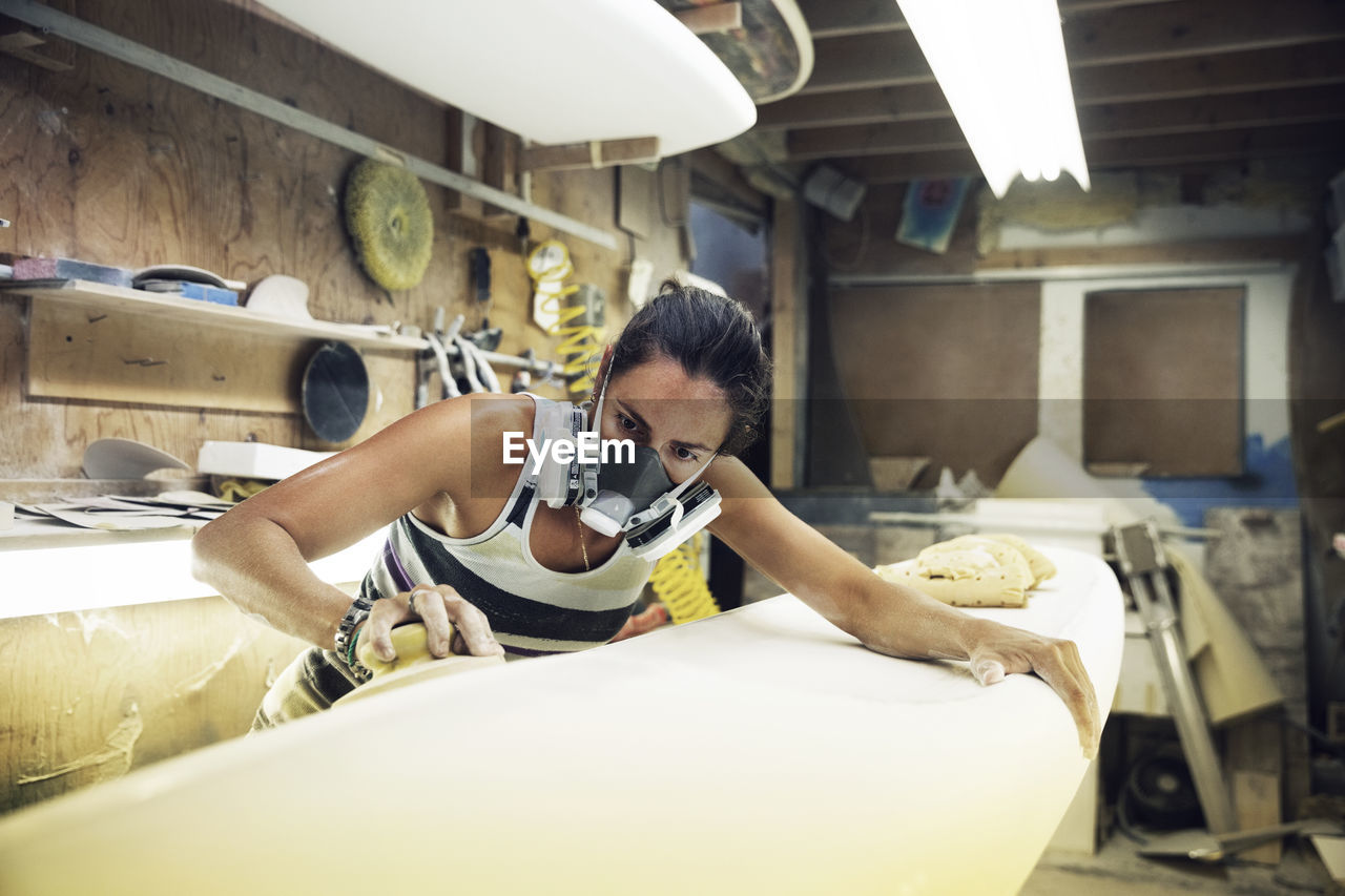 Woman shaping surfboard in workshop