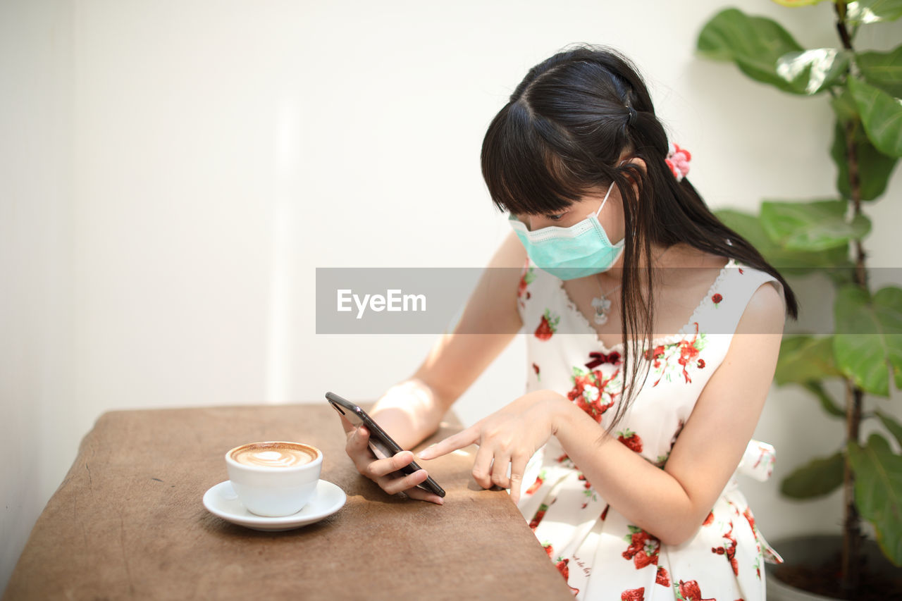 Woman wearing mask using mobile phone at table