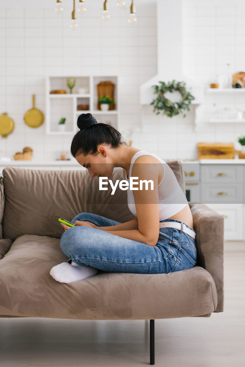 Young woman holds a smartphone in her hands, hunched over sitting on the couch