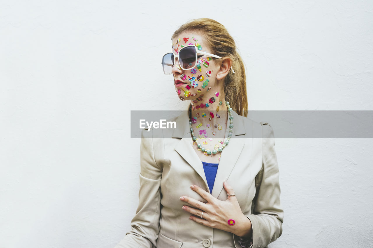 Woman with colorful stickers on face wearing sunglasses in front of white background