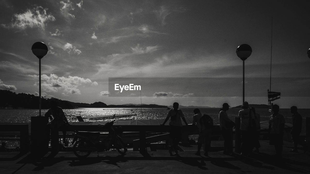 PEOPLE SITTING AT STREET BY SEA AGAINST SKY