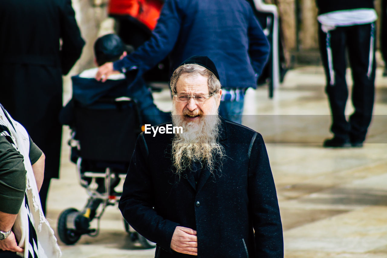 PORTRAIT OF MAN WITH PEOPLE STANDING IN THE BACKGROUND