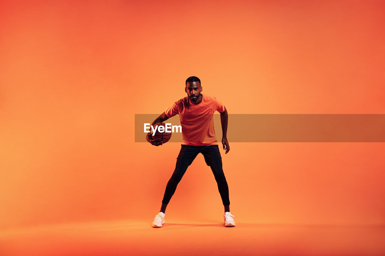 Man with basketball standing against orange background