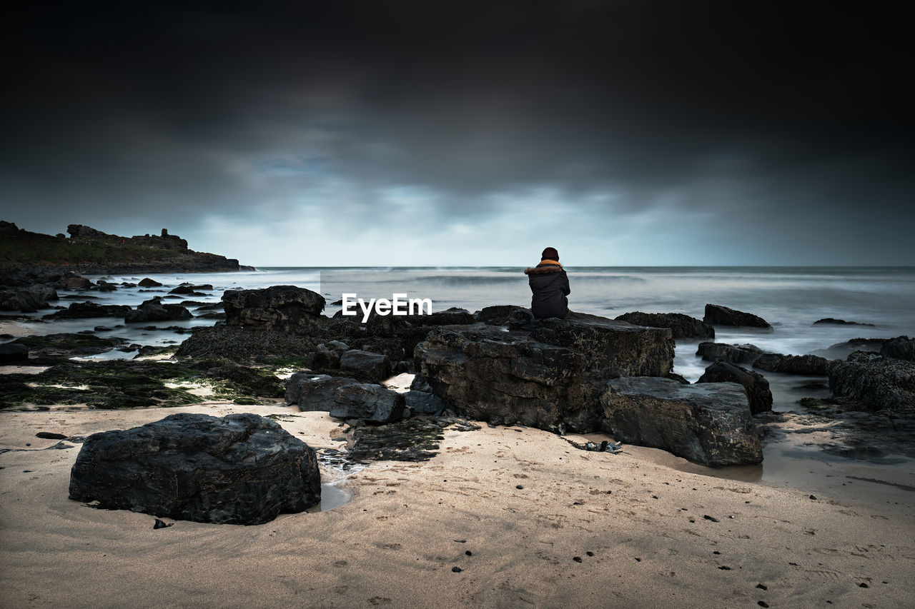 Girl in black looking out to sea sitting on rocks