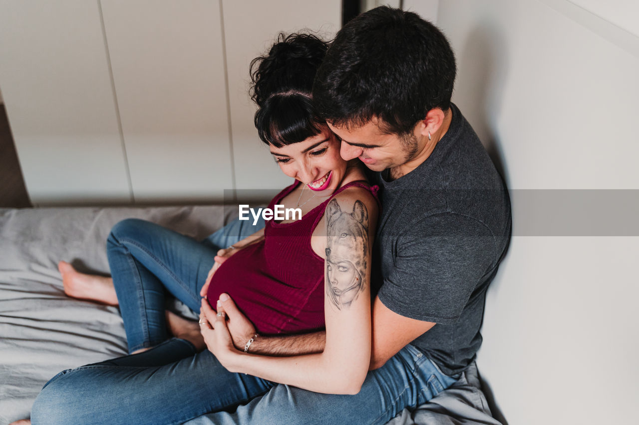 High angle view of pregnant woman sitting with male partner on bed at home