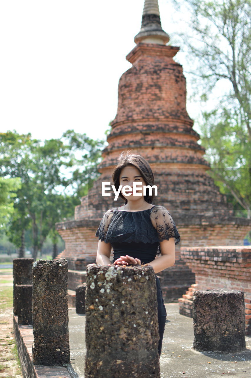 Portrait of young woman standing against old ruin temple