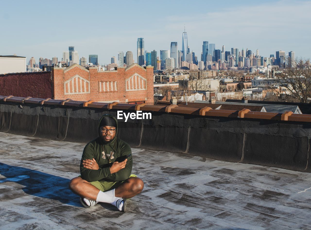 PORTRAIT OF MAN SITTING AGAINST BUILDINGS IN CITY AGAINST SKY