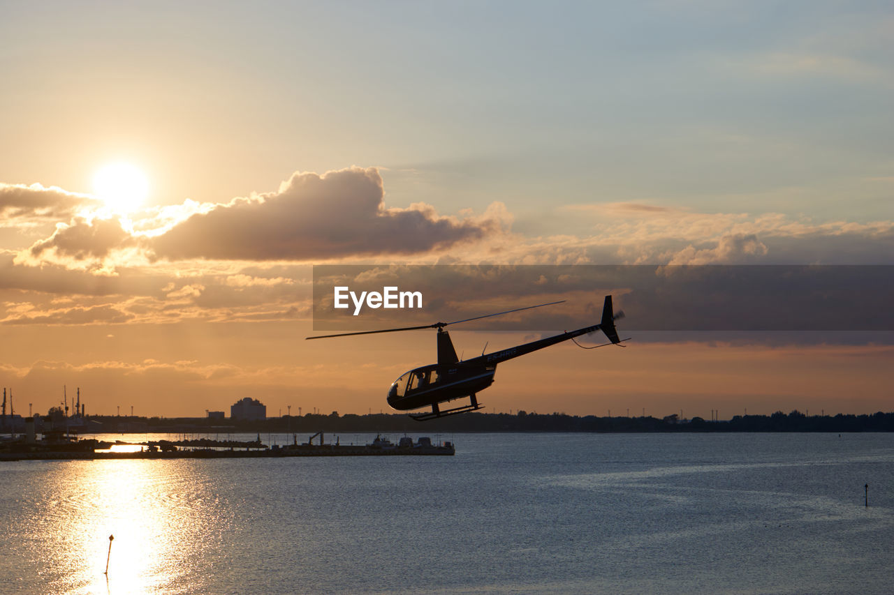 Helicopter flying over river against sky during sunset