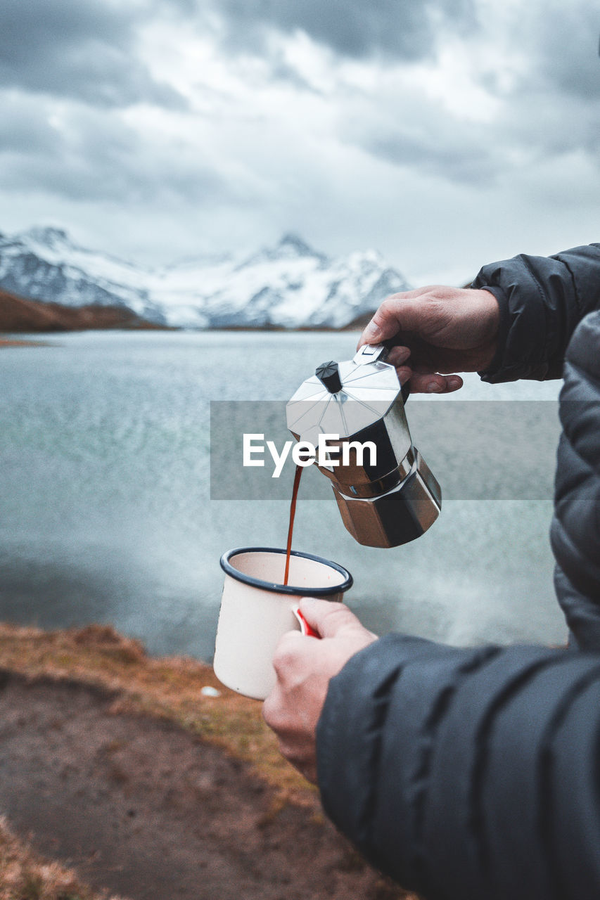 Cropped image of hand holding coffee cup against sea