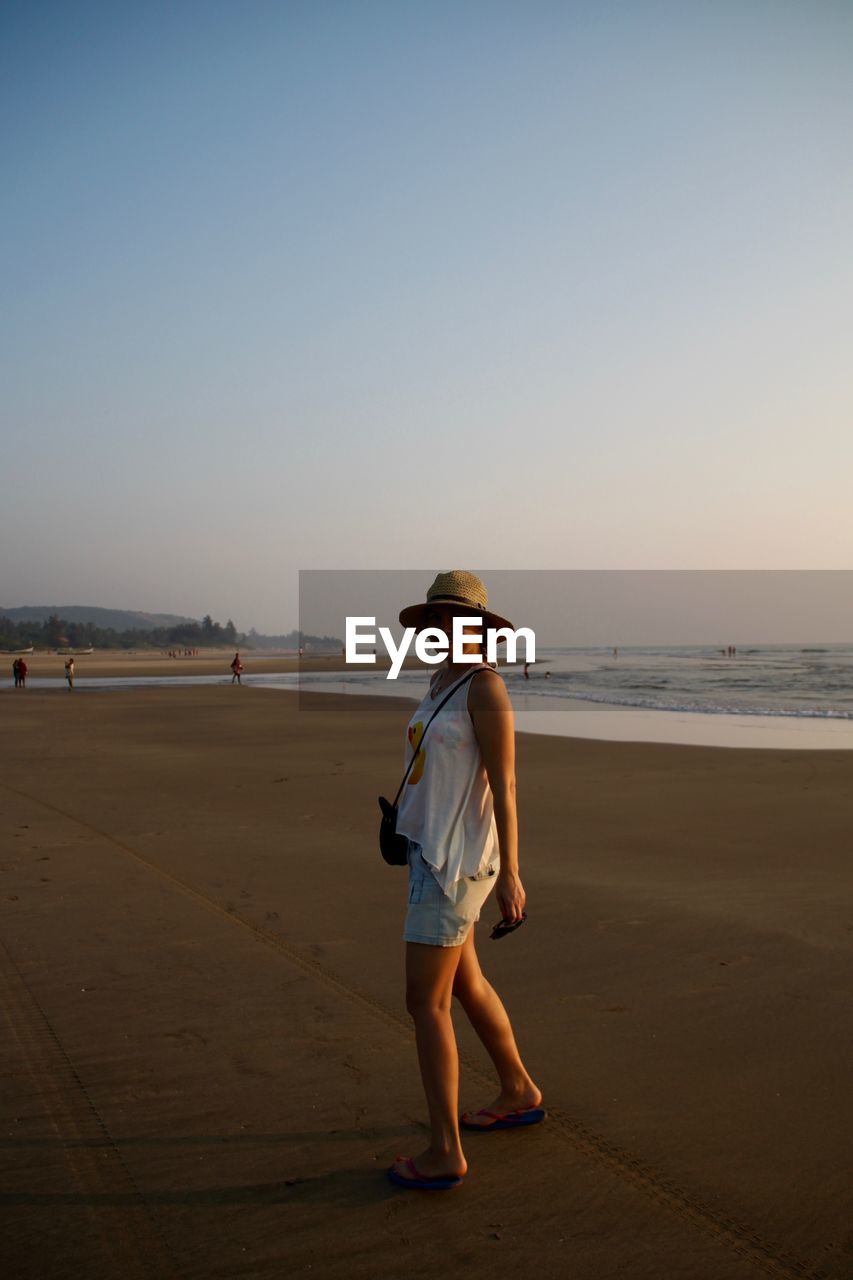 Full length of woman standing at beach against clear sky during sunset