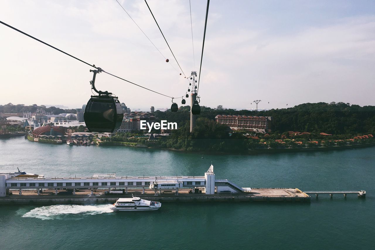 Overhead cable cars over lake against sky in city