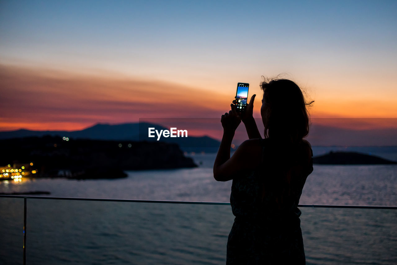 MAN PHOTOGRAPHING USING MOBILE PHONE AGAINST SKY