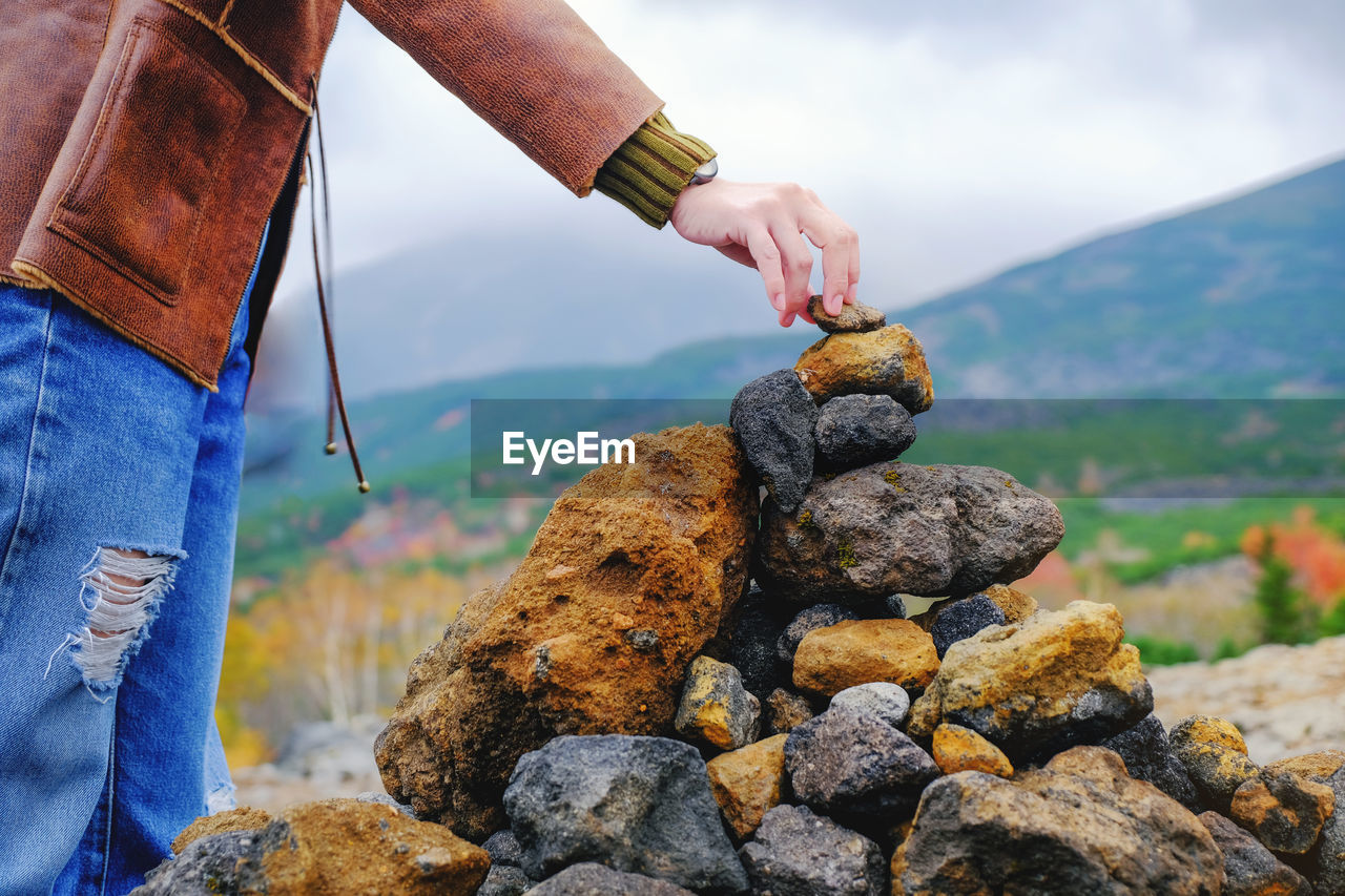Midsection of person stacking rocks against mountain