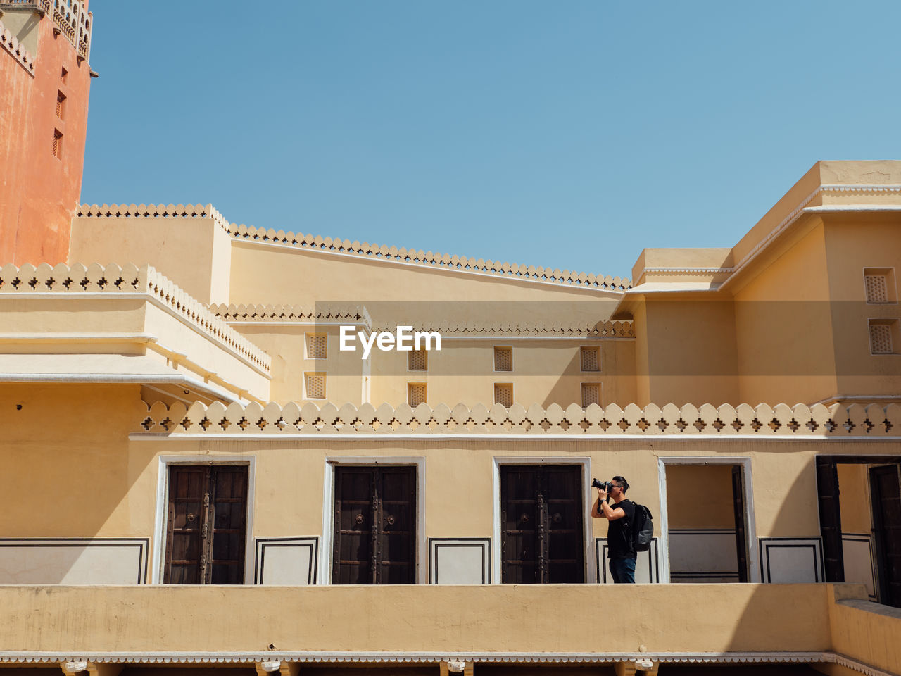 Man photographing while standing in balcony against clear sky