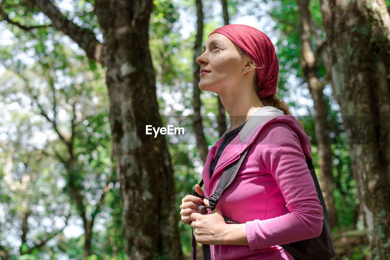 MID ADULT WOMAN LOOKING AWAY WHILE SITTING ON TREE TRUNK