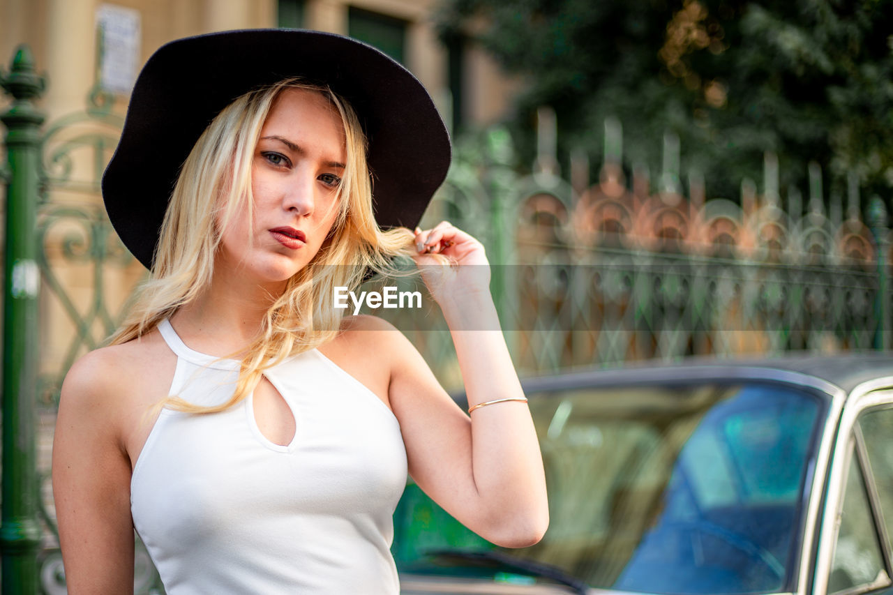 A young blond woman posing on a car on the street. female fashion model with classy outfit and car.