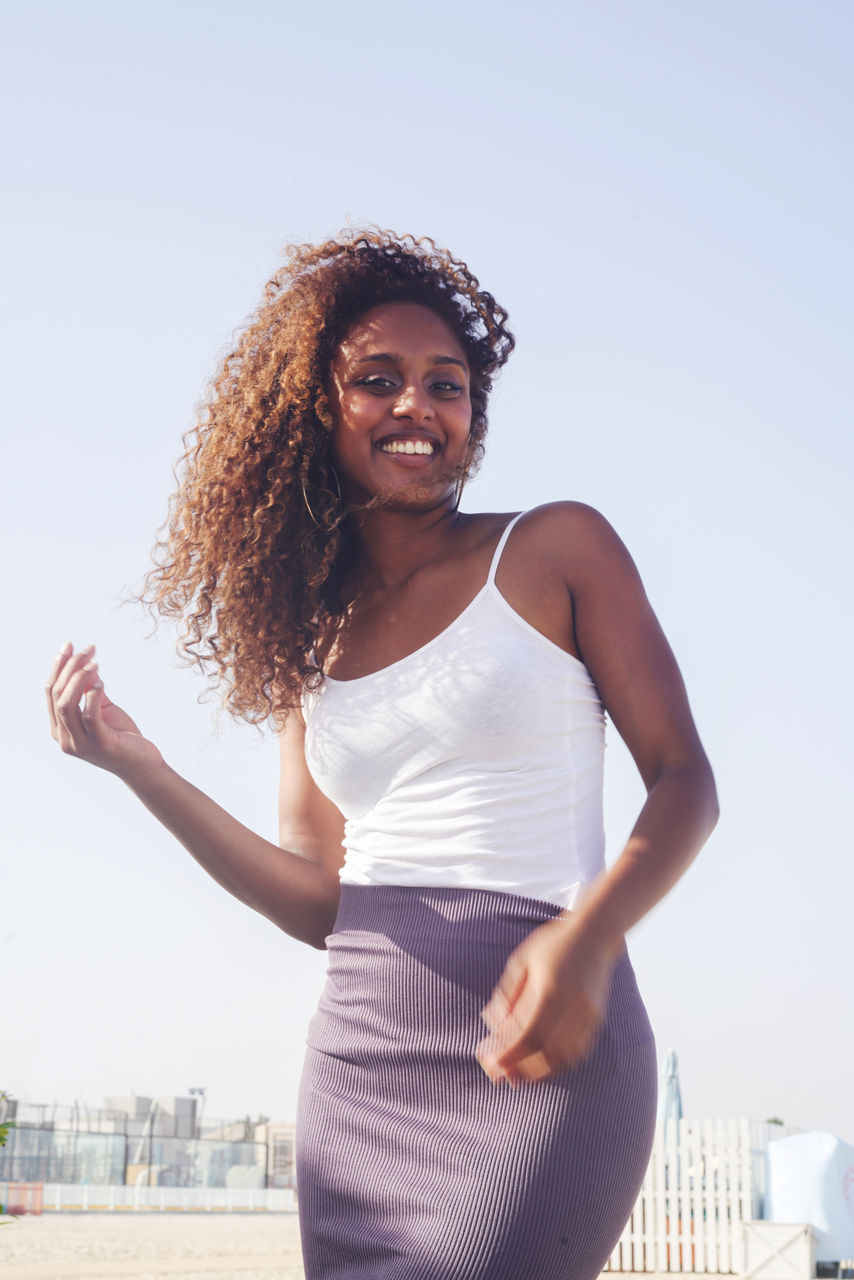 Low angle muted colors portrait of a young black woman with long curly hair