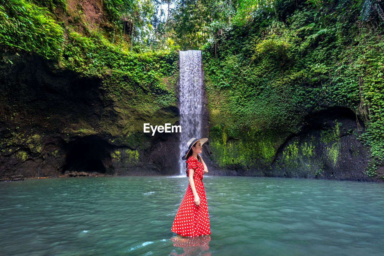 WOMAN STANDING BY ROCK AGAINST WATERFALL