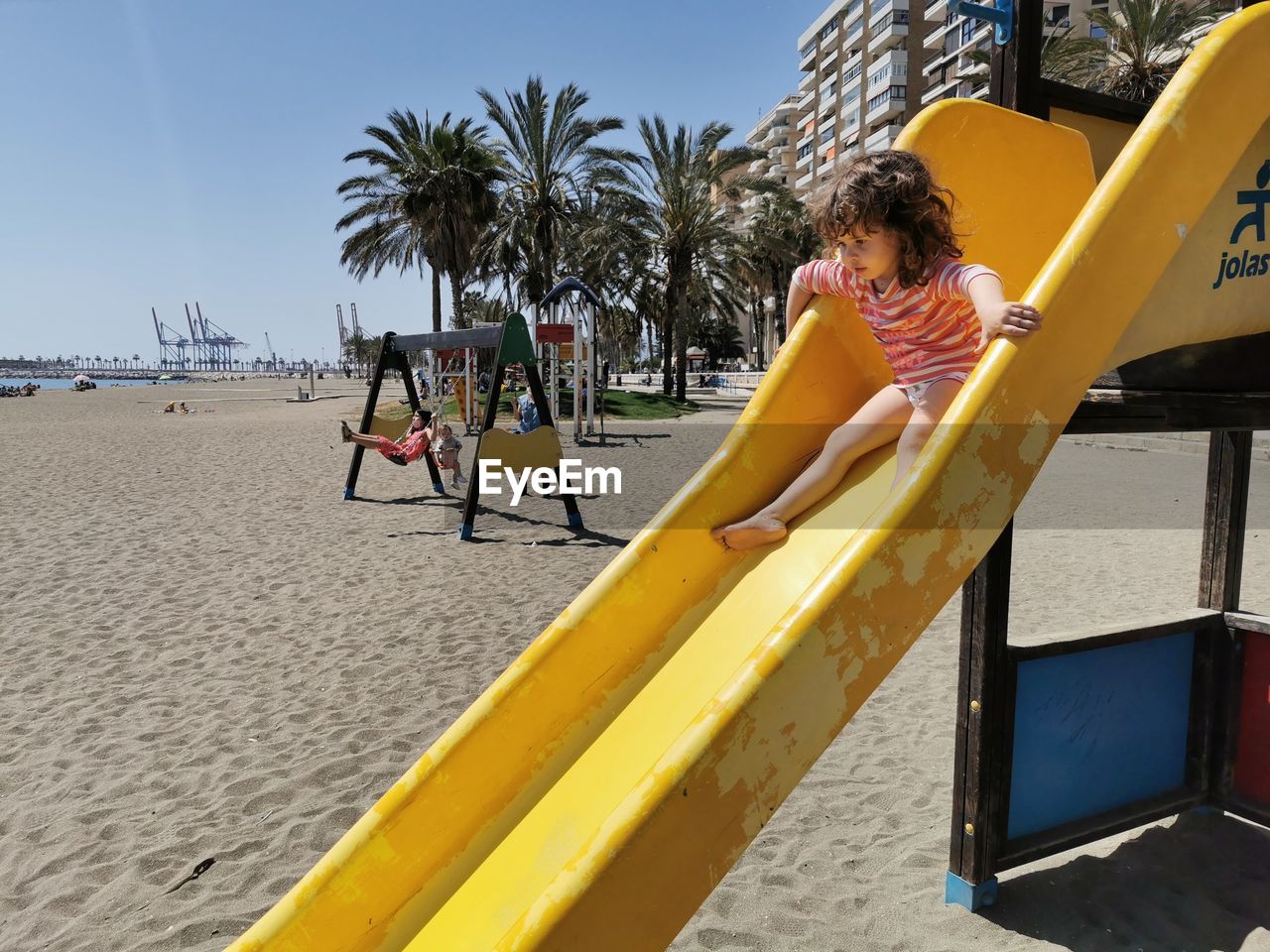  view of small girl going down the beach playground slide in summer.