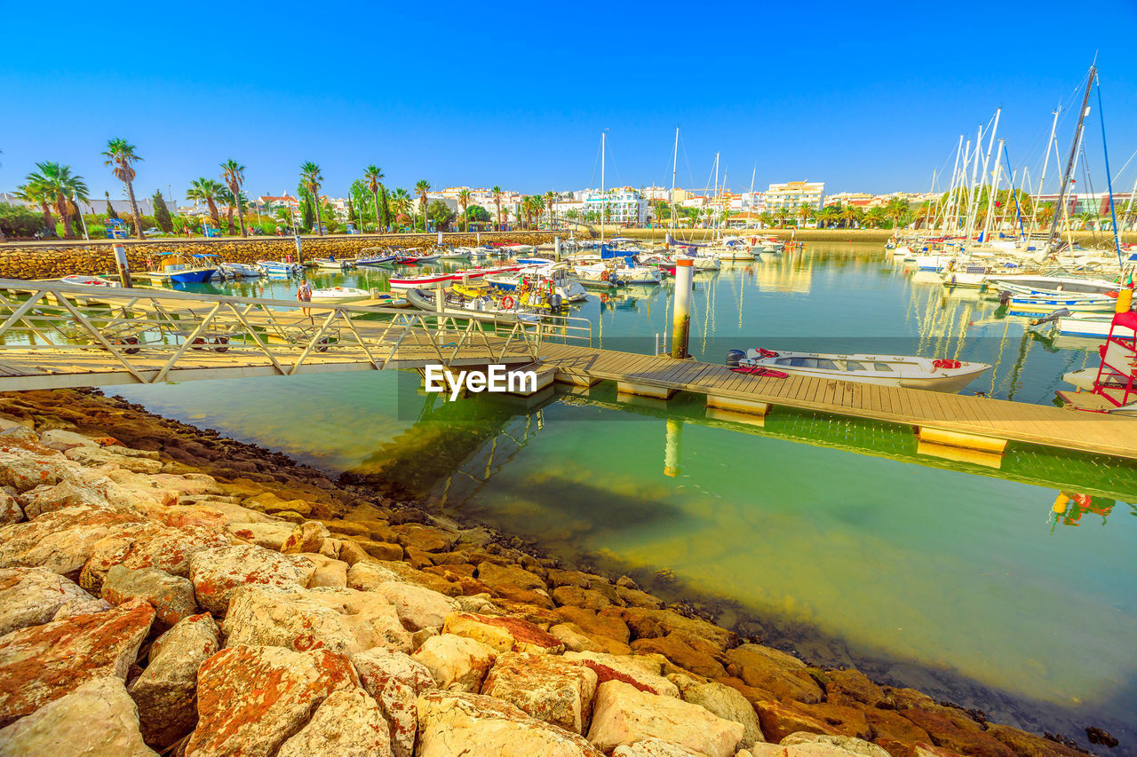 SAILBOATS MOORED ON HARBOR AGAINST CLEAR BLUE SKY